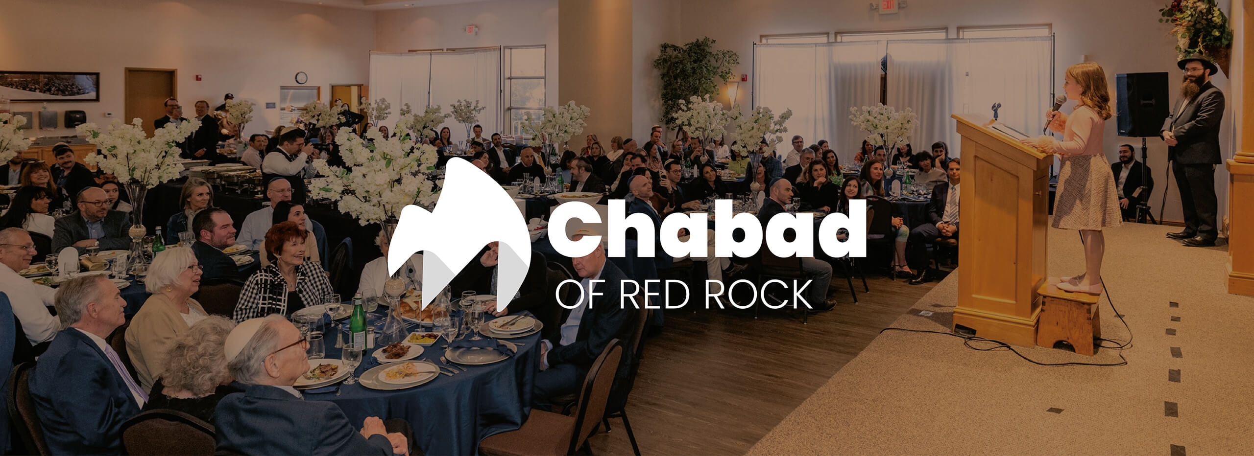 Logo de Chabad of Red Rock en blanco sobre la fotografía de un evento comunitario